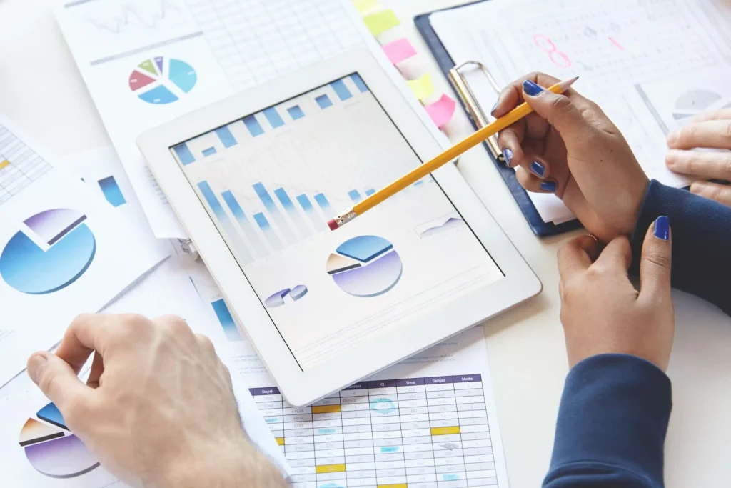 A group of business individuals engaged with a tablet, examining graphs and discussing papers in a professional environment.