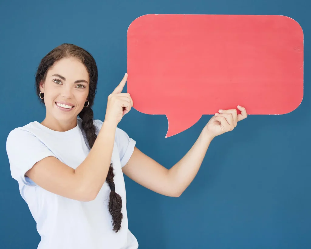 Person holding a large red speech bubble sign, pointing at it.