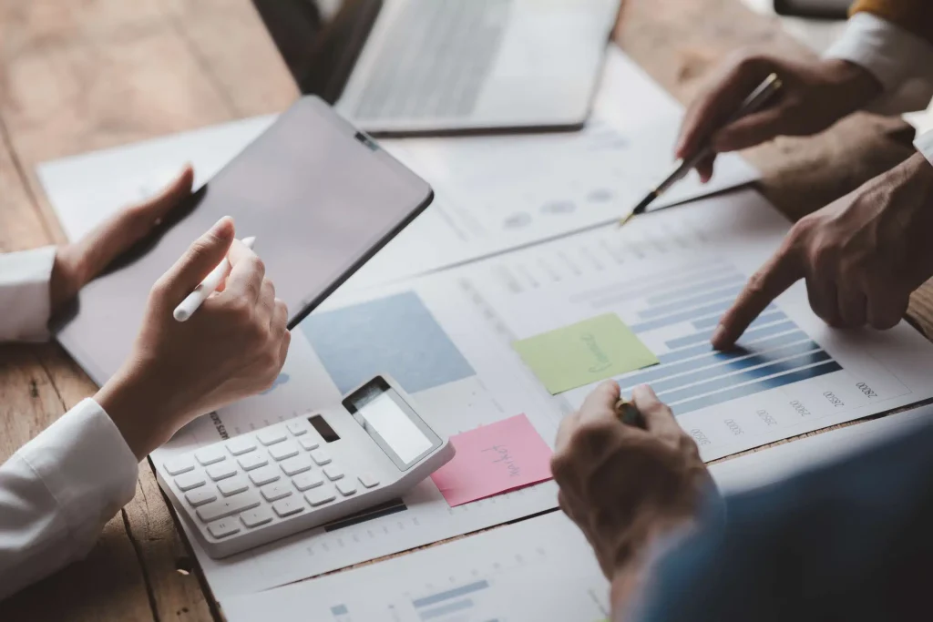 A group of business professionals collaborating on a laptop and reviewing documents in a modern office setting.