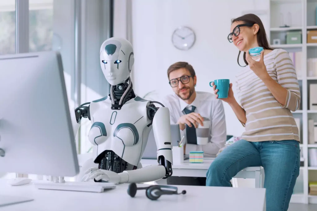A woman and a man at a desk, collaborating with a robot that is situated in front of them.