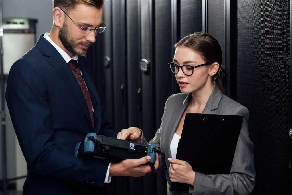 A professional man and woman in business attire focus on a computer screen, engaged in a work-related discussion.