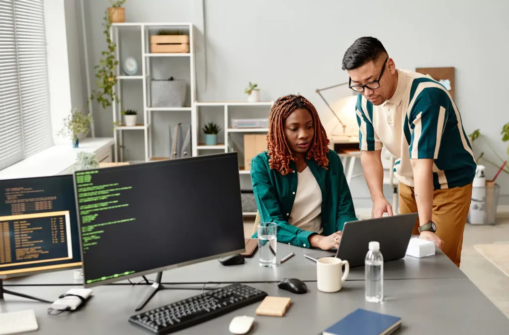 Two individuals collaborating on a computer in a modern office setting, focused on their work.