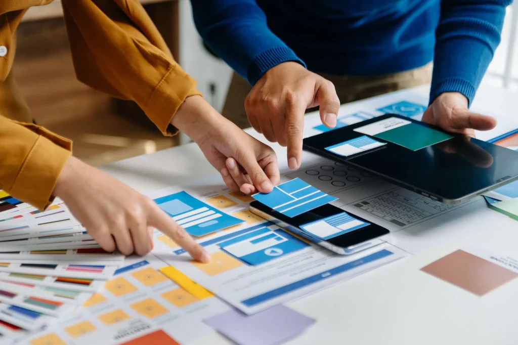 Two people focused on a laptop, with an array of colorful paper scattered around them, symbolizing teamwork and creativity.